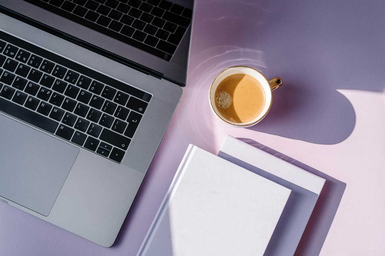 A laptop with a cup of coffee and a book on a pink table. A laptop with a cup of coffee and a book on a pink table.